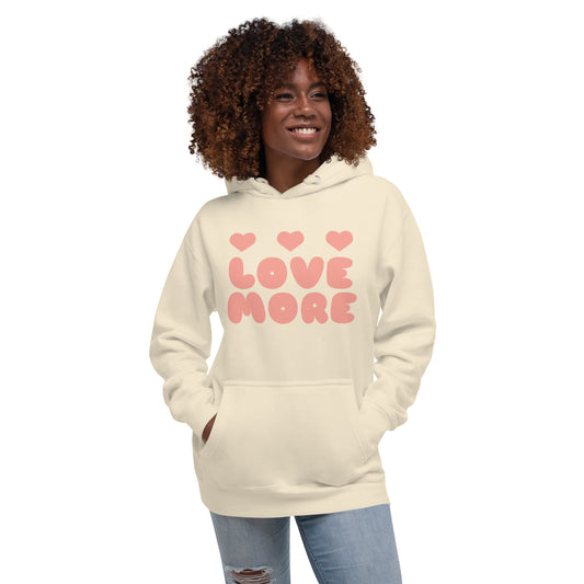 Woman wearing a beige hoodie with 'LOVE MORE' text and heart symbols on a white background