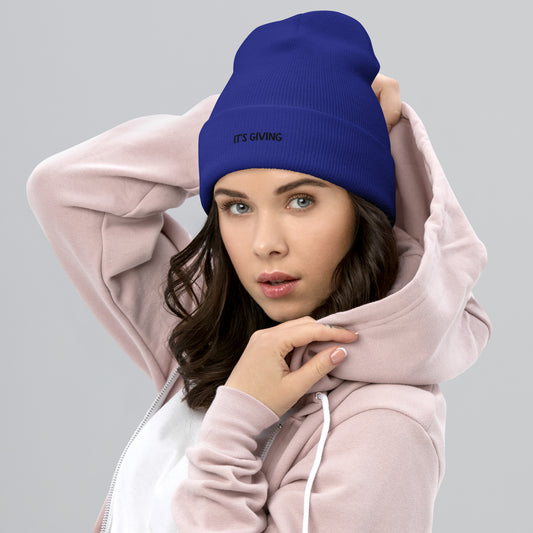 Woman wearing a blue beanie with text and a pink hoodie on a gray background